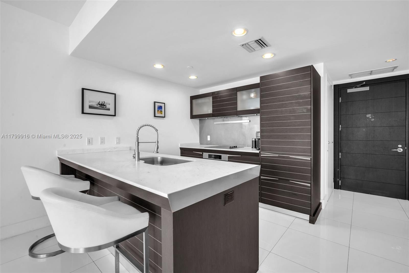 A modern kitchen features dark wood cabinetry, white countertops, and a central island with seating — 200 Biscayne Boulevard Way # 4012, Miami FL 33131, MIAMI, FL