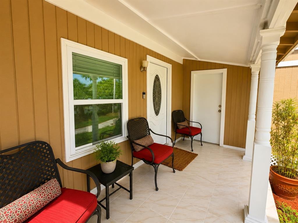 A covered front porch features tiled flooring, a white front door, and outdoor seating — 802 JURGENS STREET, CLEARWATER, FL