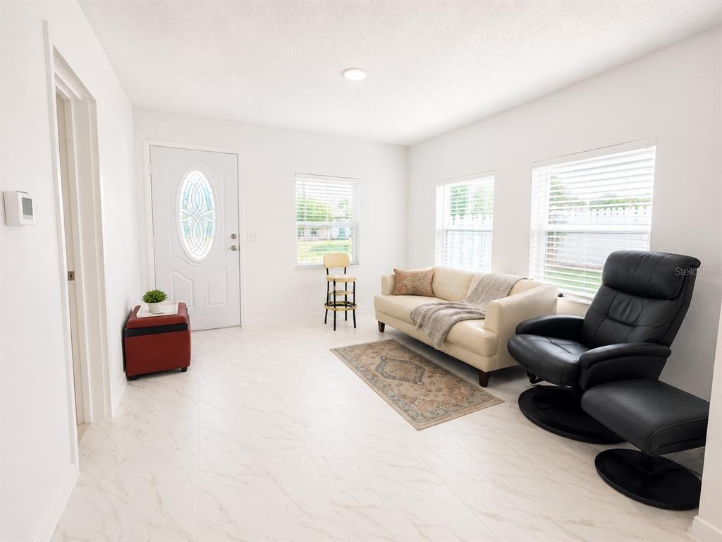 A bright living room features white tile floors, a cream sofa, and a black recliner — 802 JURGENS STREET, CLEARWATER, FL