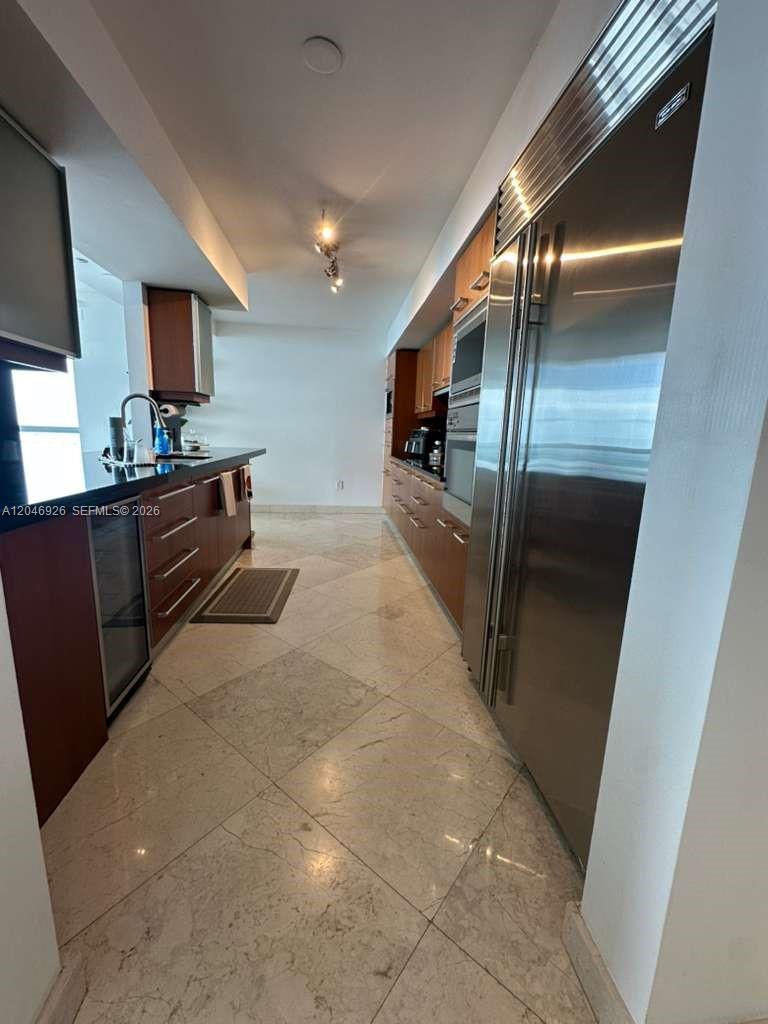 A modern kitchen features dark wood cabinetry, stainless steel appliances, and light-colored stone flooring — 1331 Brickell Bay Dr # 1911, Miami FL 33131, MIAMI, FL