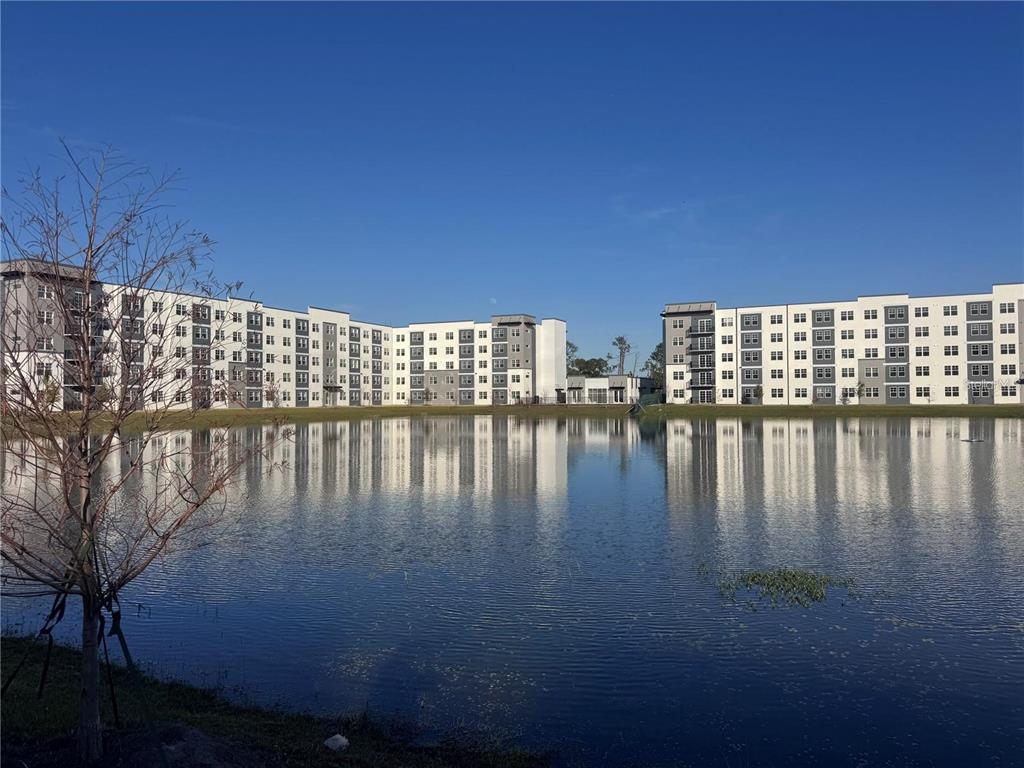 A modern multi-story apartment building exterior with white and gray siding under a clear sky — 5592 NE PGA BOULEVAR UNIT #314, ORLANDO, FL