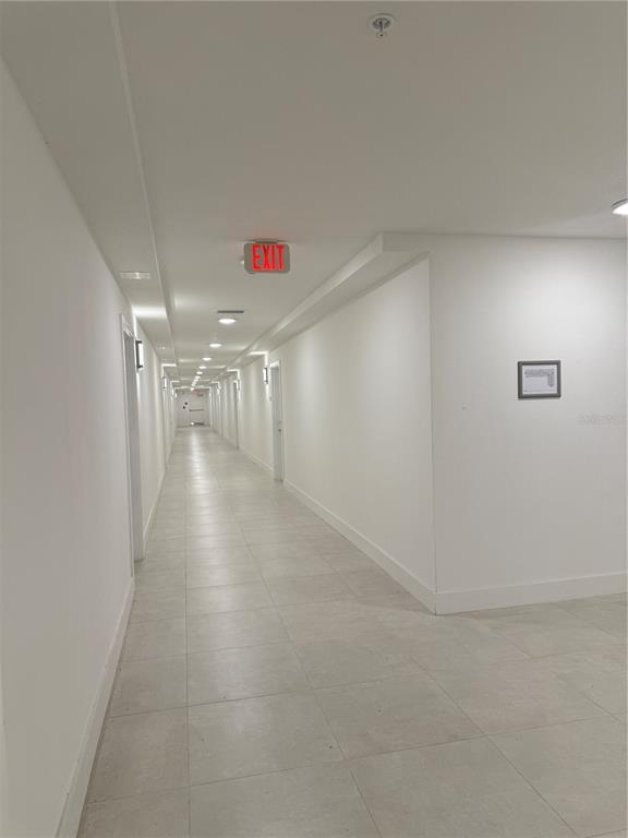 A long, brightly lit apartment hallway with white walls, tiled floors, and multiple doors — 5592 NE PGA BOULEVAR UNIT #314, ORLANDO, FL