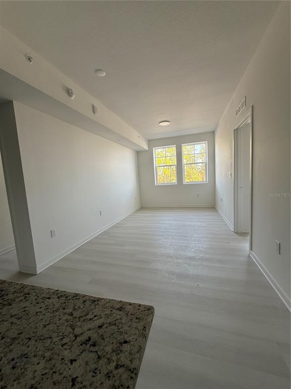 An empty room with light wood-look flooring, white walls, and two windows — 5592 NE PGA BOULEVAR UNIT #314, ORLANDO, FL