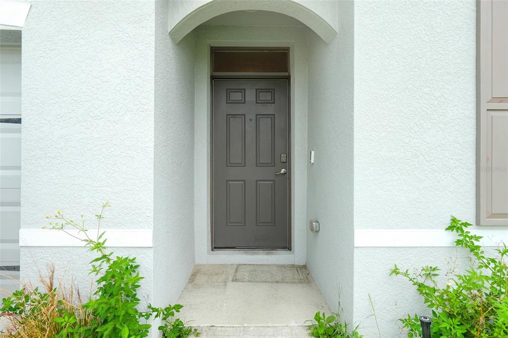 A gray front door with a transom window is set within a recessed entryway — 658 COTULLA DRIVE, KISSIMMEE, FL