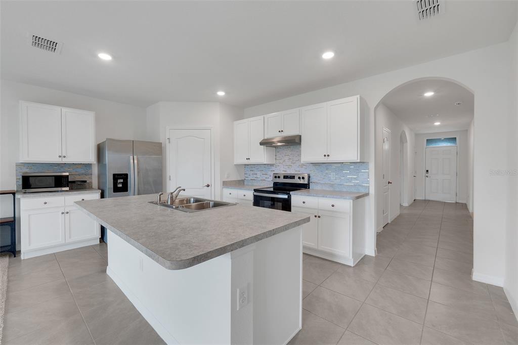 A kitchen with white cabinets, a gray island, stainless steel appliances, and light tile flooring — 658 COTULLA DRIVE, KISSIMMEE, FL