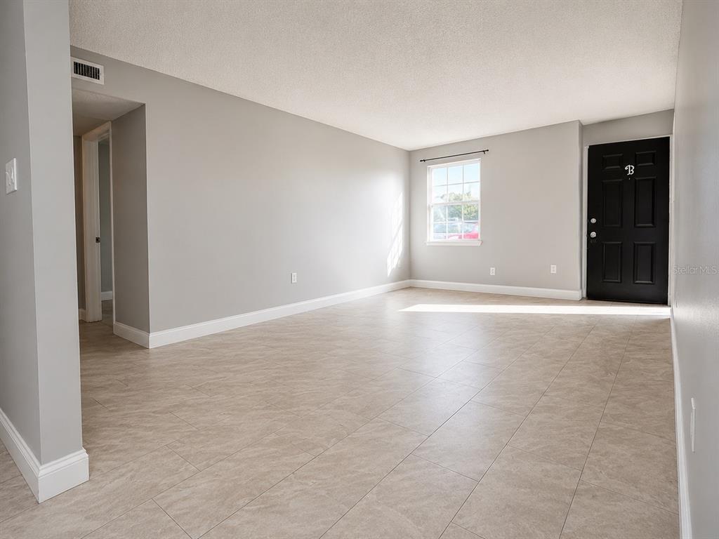 An empty living room with light gray walls, tile flooring, a window, and a black door — 2789 L B MCLEOD ROAD UNIT 2789B, ORLANDO, FL