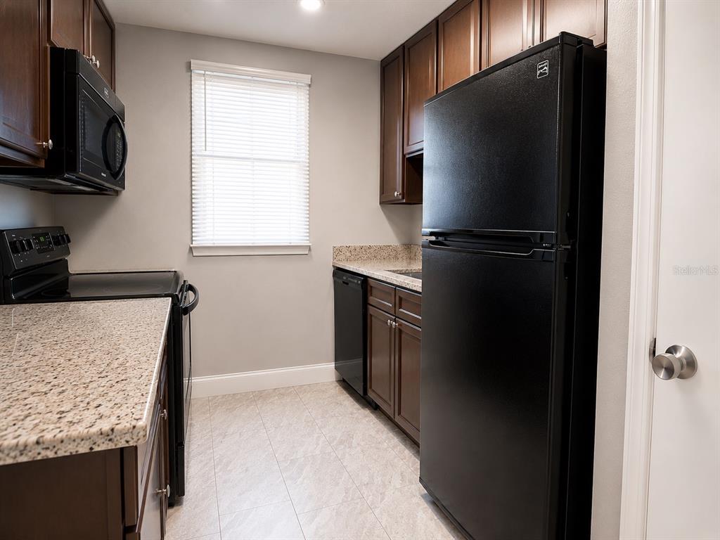 A kitchen features dark wood cabinets, granite countertops, black appliances, and light-colored tile flooring — 2789 L B MCLEOD ROAD UNIT 2789B, ORLANDO, FL