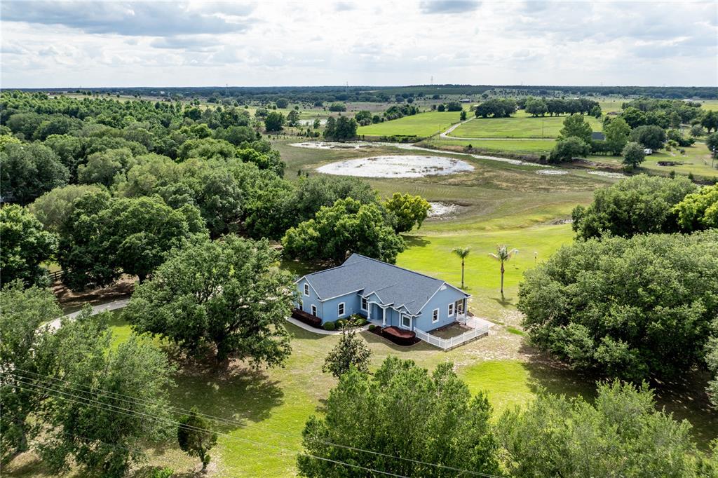 An aerial view shows a blue house with a dark roof surrounded by trees — 25101 TURKEY LAKE ROAD, HOWEY IN THE HILLS, FL