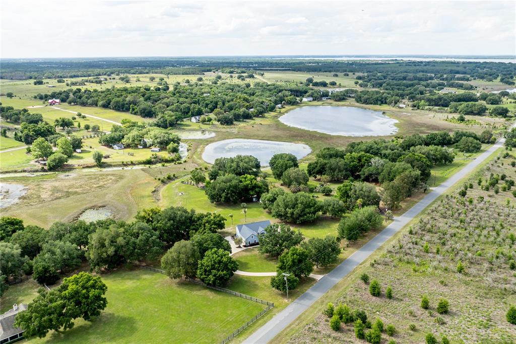 An aerial view shows a house surrounded by trees, green fields, and two small lakes — 25101 TURKEY LAKE ROAD, HOWEY IN THE HILLS, FL