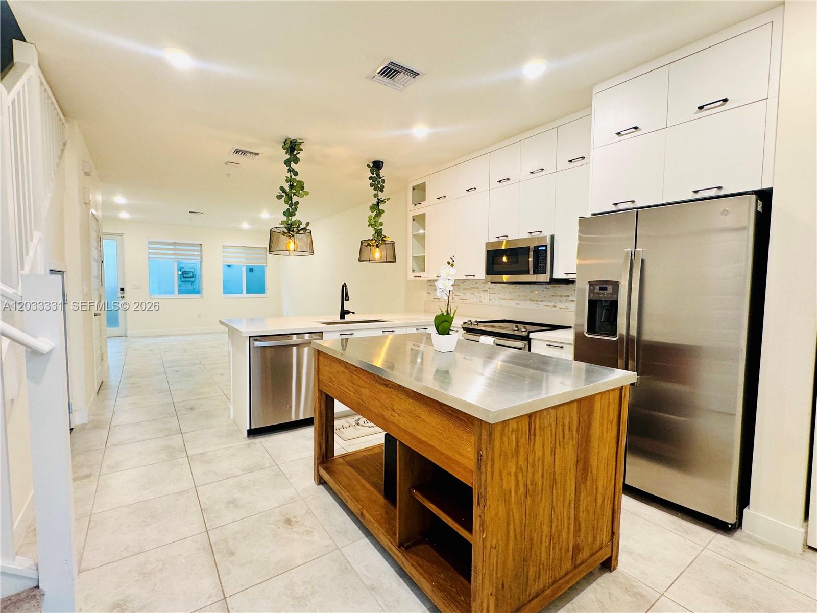 A kitchen features white cabinetry, stainless steel appliances, and a wooden island with metal top — 10295 NW 64th Ter # 104, Doral FL 33178, DORAL, FL