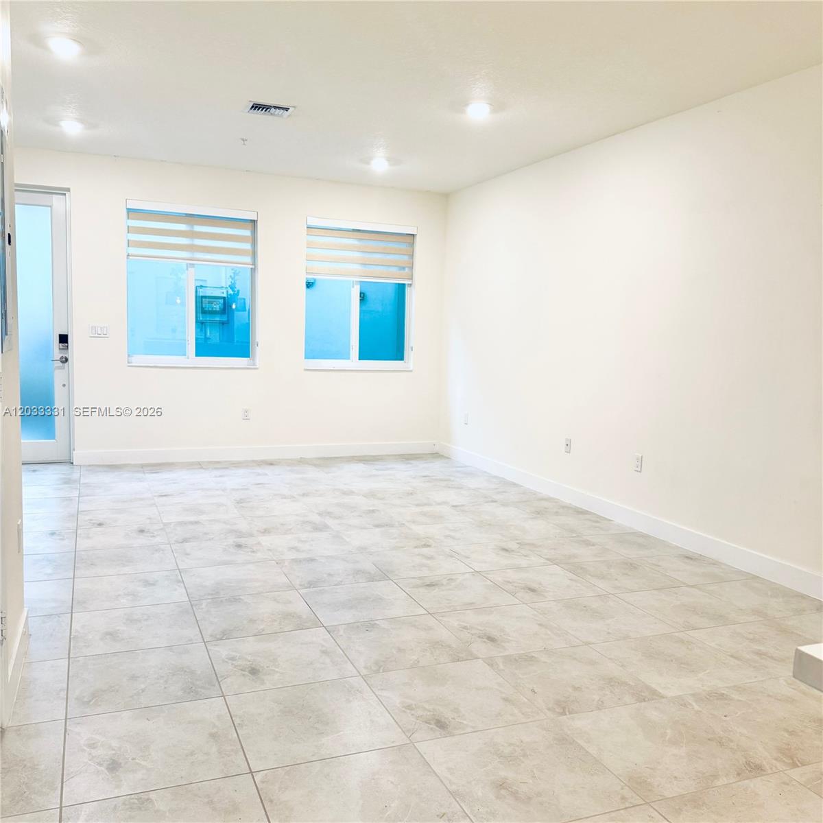 An empty room features white walls, light-colored tile flooring, recessed lighting, and two windows — 10295 NW 64th Ter # 104, Doral FL 33178, DORAL, FL