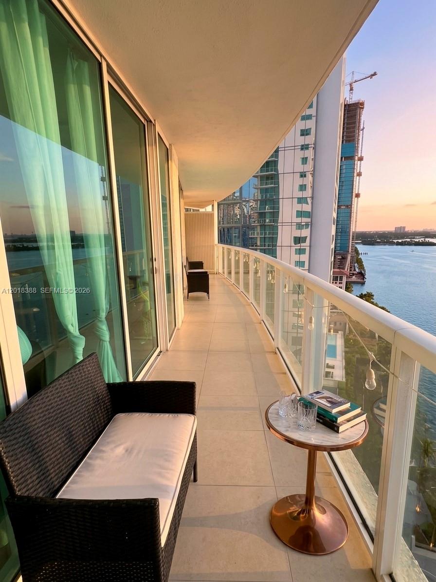 A high-rise balcony features a wicker sofa, a small round table, and glass railings — 665 NE 25th St # 1404, Miami FL 33137, MIAMI, FL