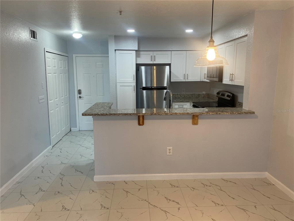 A kitchen with white cabinets, stainless steel appliances, and a granite-topped breakfast bar — 13838 FAIRWAY ISLAND DRIVE UNIT 1413, ORLANDO, FL
