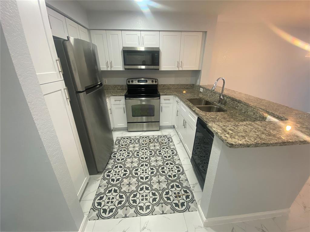 A kitchen features white cabinets, stainless steel appliances, granite countertops, and a patterned floor inlay — 13838 FAIRWAY ISLAND DRIVE UNIT 1413, ORLANDO, FL