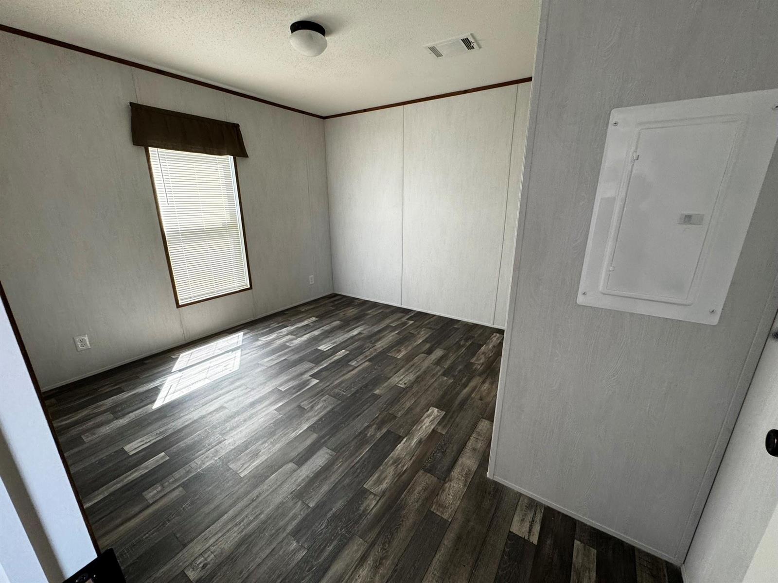 An empty room features wood-look vinyl flooring, light-colored paneled walls, and a white electrical panel — 8791 Highway 78, Okeechobee FL 34971, OKEECHOBEE, FL