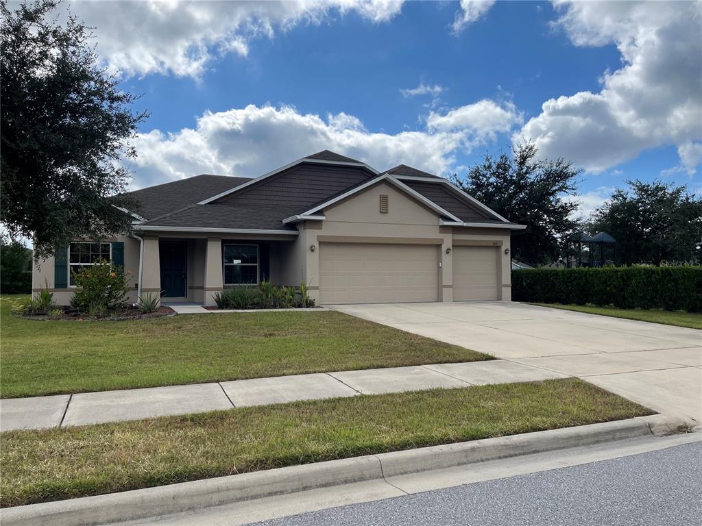 A single-story house with a beige stucco exterior, dark roof, and a three-car garage — 1312 RALPH POE DRIVE, APOPKA, FL