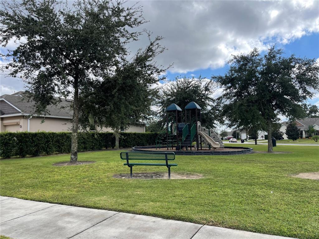 A green park bench sits on a grassy lawn in front of a playground structure — 1312 RALPH POE DRIVE, APOPKA, FL