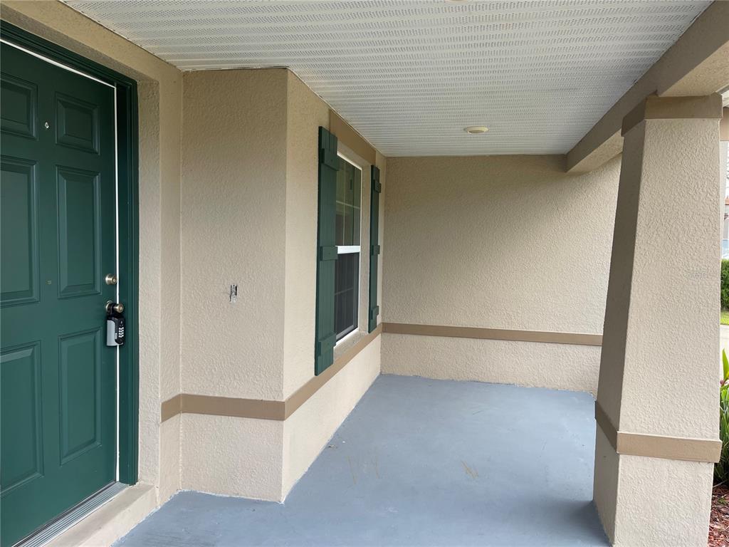 A covered front porch features a green door, a window with shutters, and painted flooring — 1312 RALPH POE DRIVE, APOPKA, FL