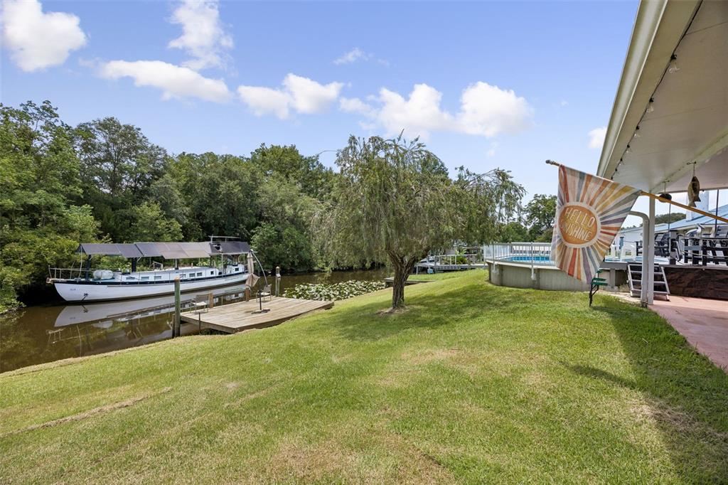A grassy backyard features a boat docked on a canal, a pool, and a patio — 134 BOWFIN DRIVE, PALATKA, FL