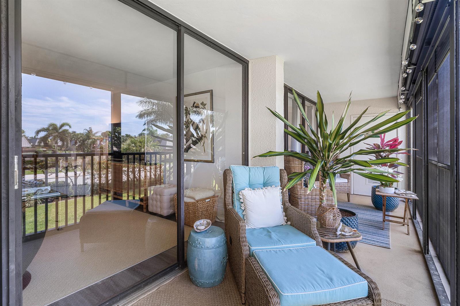 A screened-in balcony features wicker furniture with blue cushions, potted plants, and sliding glass doors — 1605 S Us Highway 1, Jupiter FL 33477, JUPITER, FL
