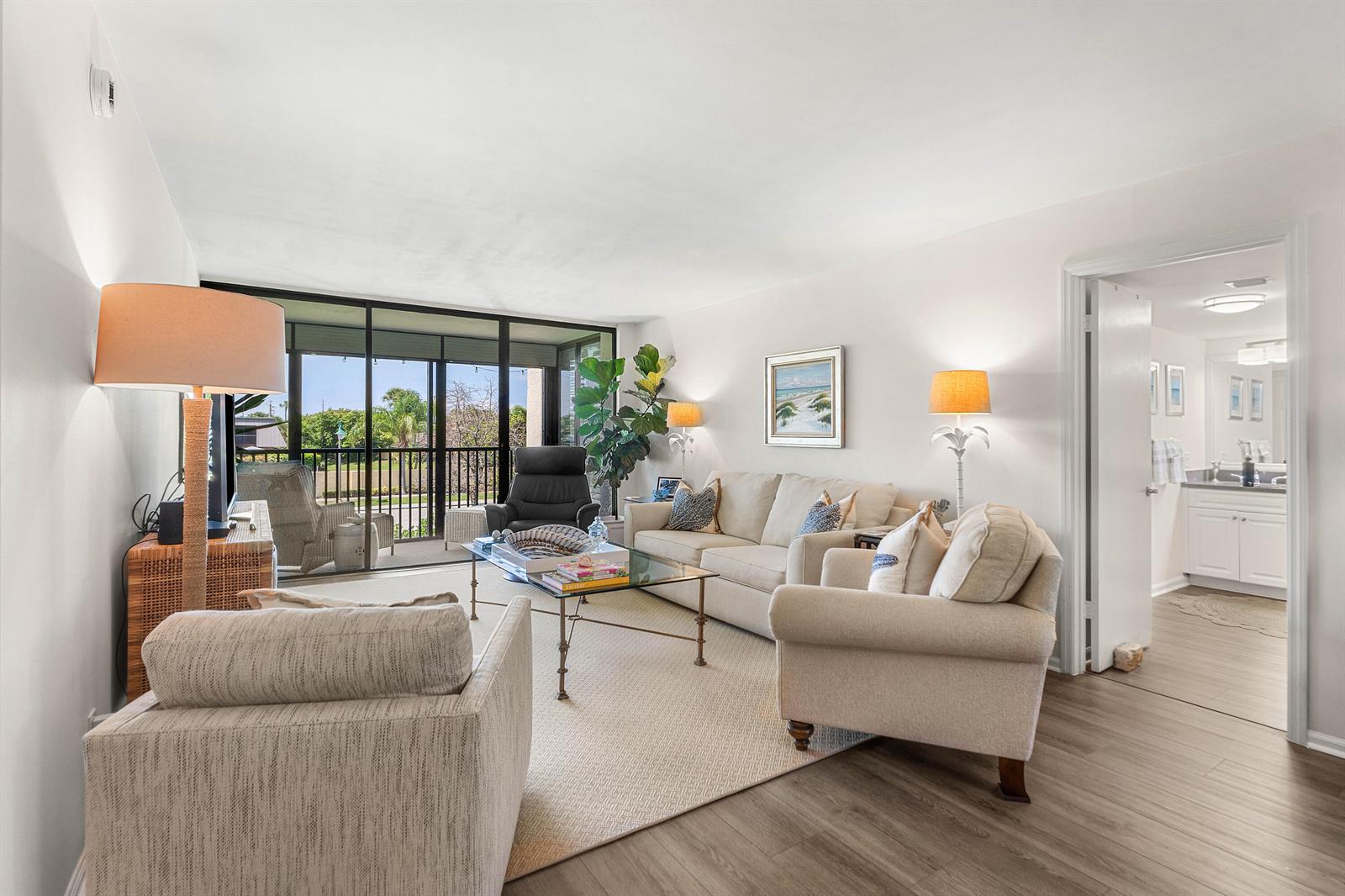 A living room features light-colored furniture, a glass coffee table, and a sliding door to a balcony — 1605 S Us Highway 1, Jupiter FL 33477, JUPITER, FL