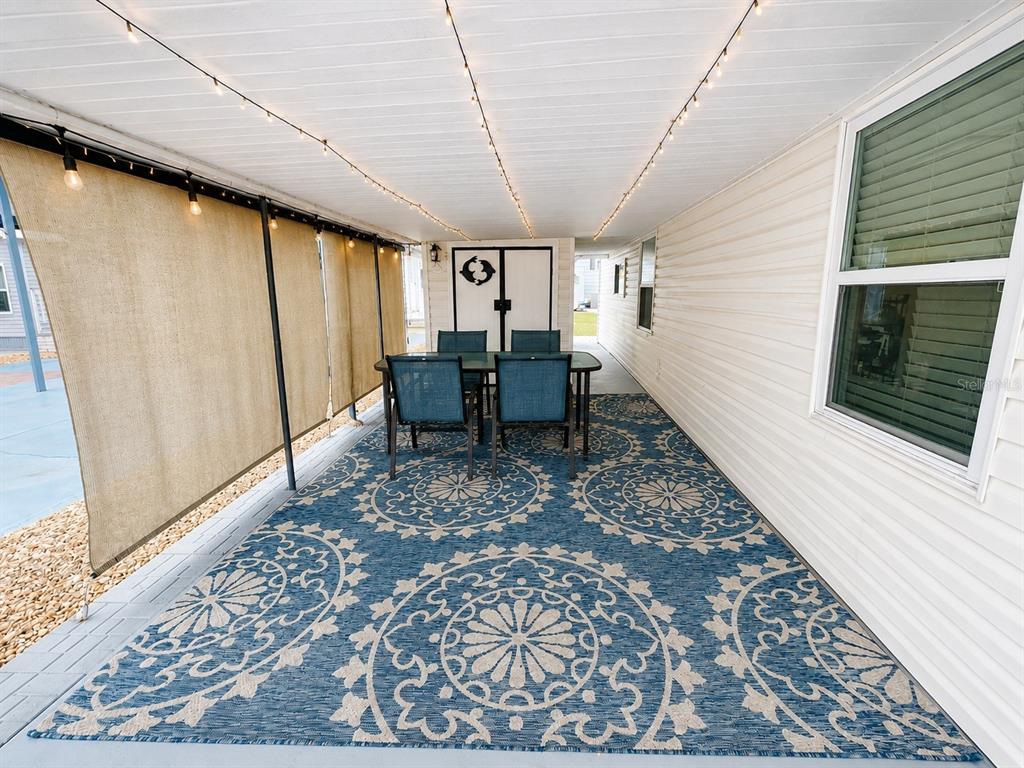 A covered outdoor patio features a blue patterned rug, dining set, and string lighting — 1907 IOWA AVENUE, BRADENTON, FL