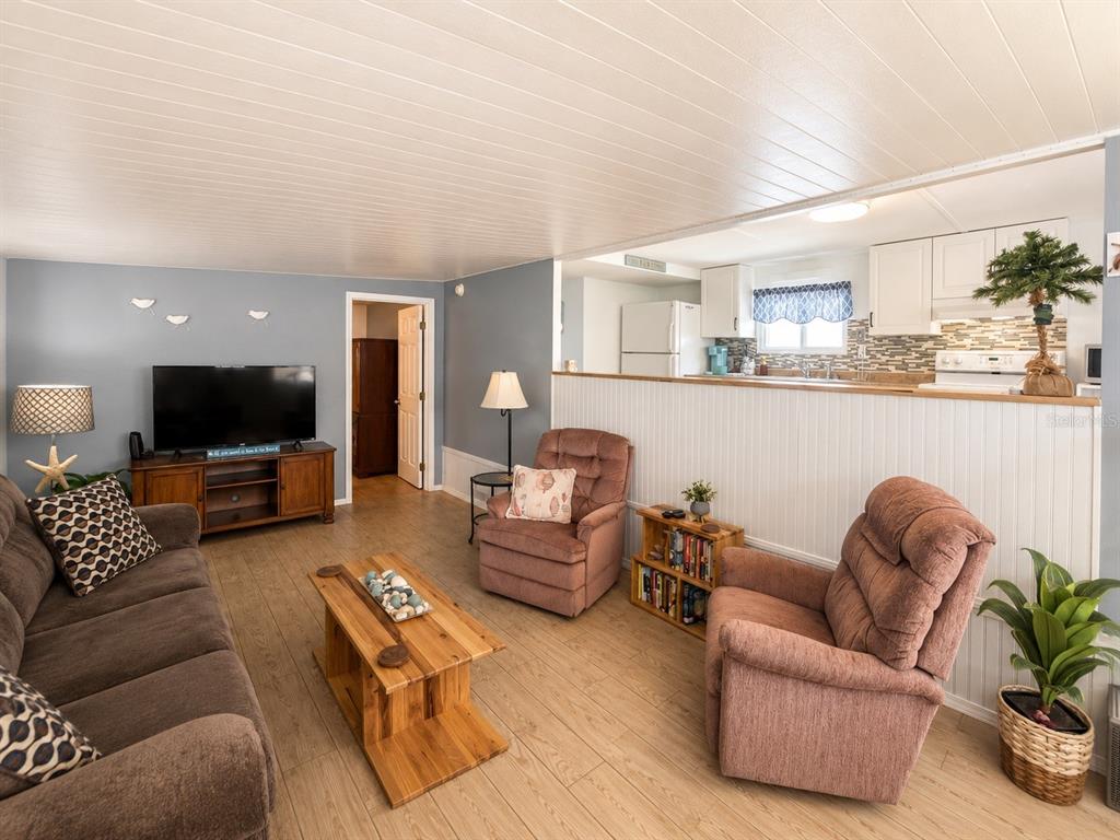 A living room with wood-look flooring, a brown sofa, two recliners, and an open kitchen — 1907 IOWA AVENUE, BRADENTON, FL