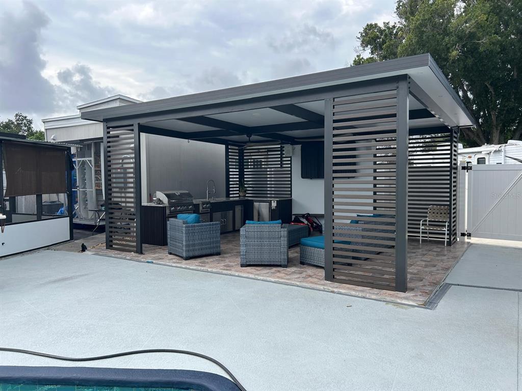 An outdoor covered patio features a kitchen, lounge seating, and slatted privacy walls — 6503 DOVEWOOD PLACE, TAMPA, FL