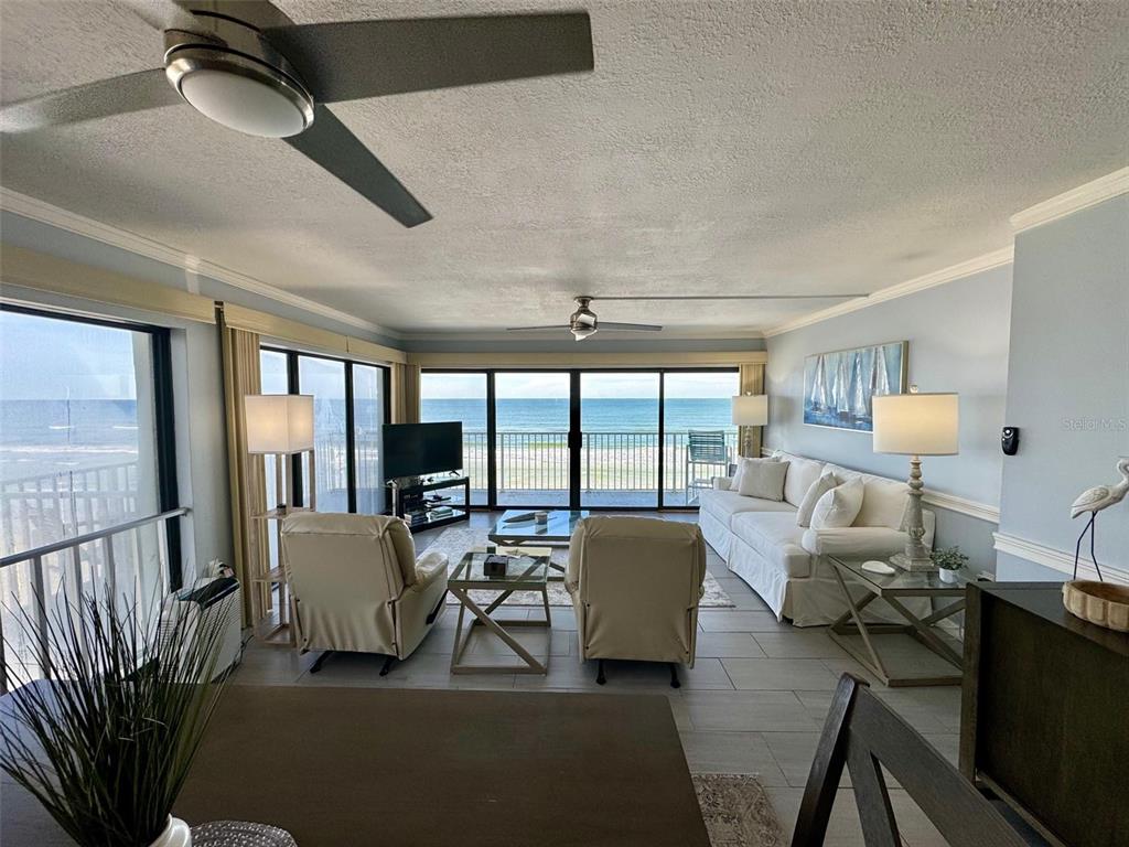 A living room with light-colored furniture, tile floors, and a balcony overlooking the ocean — 1571 S ATLANTIC AVENUE UNIT 410, NEW SMYRNA BEACH, FL