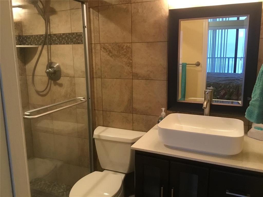 A bathroom features a glass-enclosed shower, a white vessel sink, and tan wall tiles — 1571 S ATLANTIC AVENUE UNIT 410, NEW SMYRNA BEACH, FL