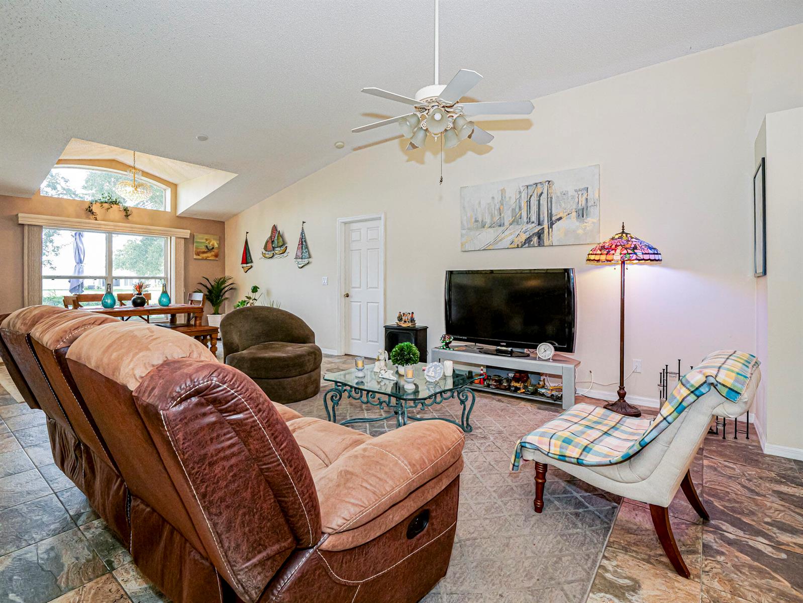 A living room features a brown leather sofa, a glass coffee table, and a ceiling fan — 1360 10th Manor, Vero Beach FL 32960, VERO BEACH, FL