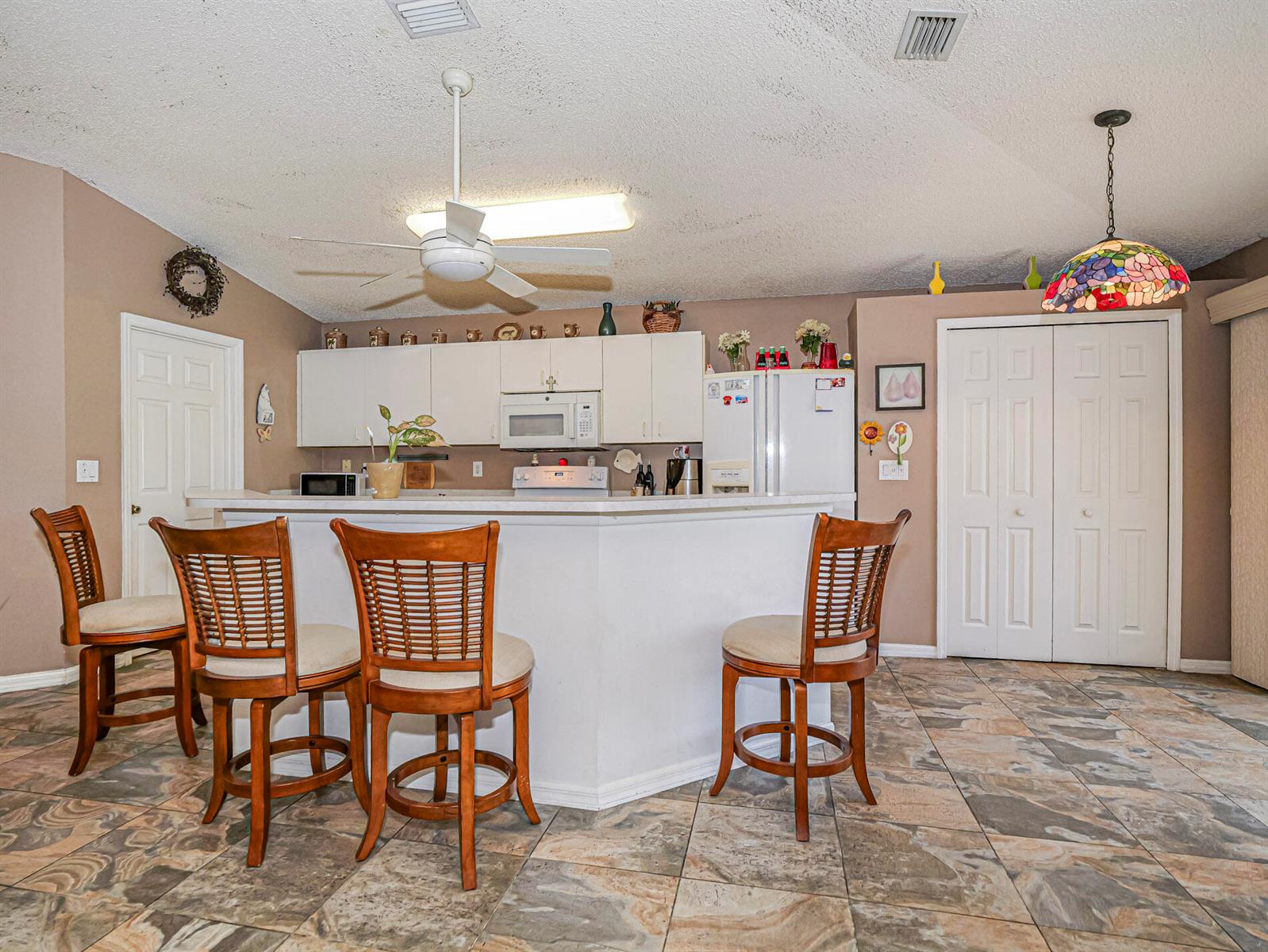 A kitchen with a breakfast bar, wooden chairs, white cabinets, and tiled flooring — 1360 10th Manor, Vero Beach FL 32960, VERO BEACH, FL