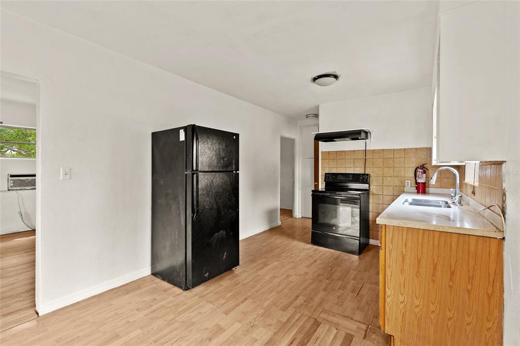 A kitchen features a black refrigerator, a black stove, wood-look flooring, and tan tiled backsplash — 4222 18TH STREET N, ST PETERSBURG, FL