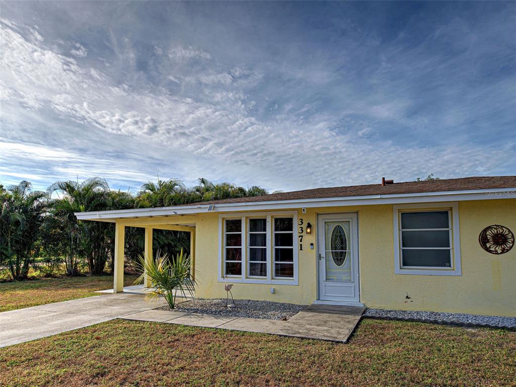 A yellow single-story house features a covered carport, a front walkway, and a glass-paneled door — 3371 PINETREE STREET, PORT CHARLOTTE, FL