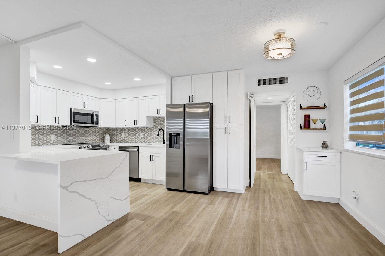 A modern kitchen features white cabinetry, stainless steel appliances, and a marble-topped island — 62 Monaco B # 62, Delray Beach FL 33446, DELRAY BEACH, FL