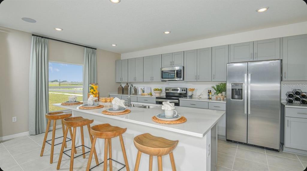 A kitchen features a large island with four wooden stools, grey cabinets, and stainless appliances — 6769 EQUINOX LANE, NORTH FORT MYERS, FL