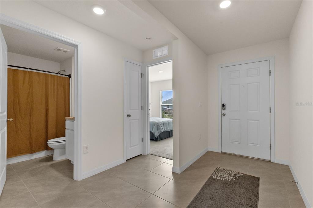 A tiled entryway features a white front door, a bathroom, and a bedroom doorway — 37207 SHARKS EYE LANE, ZEPHYRHILLS, FL