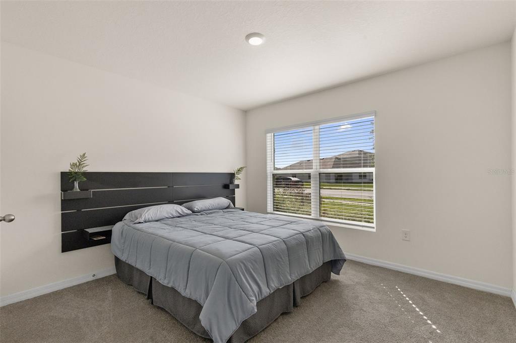 A bedroom features a gray bed with a black headboard and a window with blinds — 37207 SHARKS EYE LANE, ZEPHYRHILLS, FL