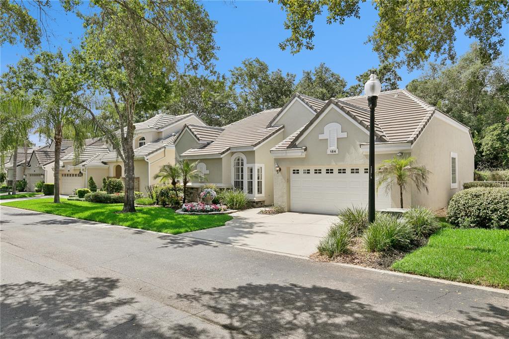 A single-story suburban house with a beige stucco exterior, tiled roof, and two-car garage — 184 WIMBLEDON CIRCLE, LAKE MARY, FL