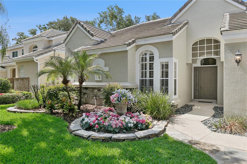 A beige house exterior features a stone-bordered flower bed, a palm tree, and a walkway — 184 WIMBLEDON CIRCLE, LAKE MARY, FL