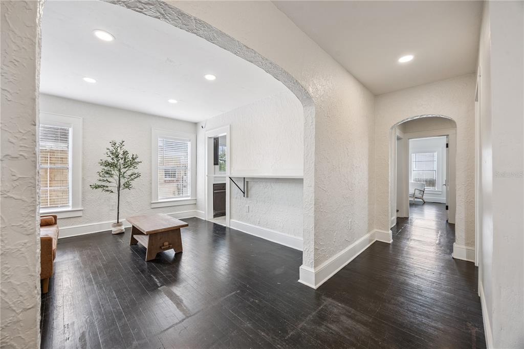 A living room with dark hardwood floors, white textured walls, and an arched entryway — 25 E PINECREST AVENUE, EUSTIS, FL