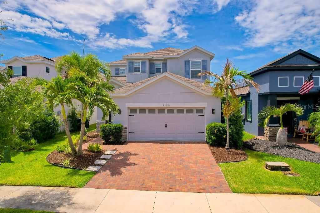 A two-story suburban house with a brick driveway, a two-car garage, and palm trees — 6135 VOYAGERS PLACE, APOLLO BEACH, FL