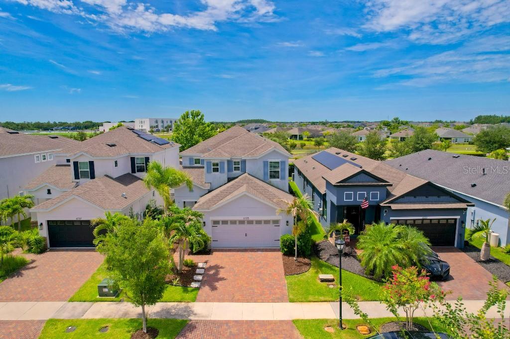 An aerial view shows three suburban houses with paved driveways and green lawns — 6135 VOYAGERS PLACE, APOLLO BEACH, FL