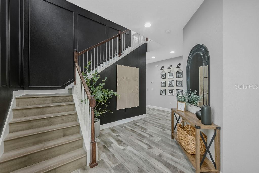 A foyer features a staircase with black paneled walls, wood-look flooring, and a console table — 6135 VOYAGERS PLACE, APOLLO BEACH, FL