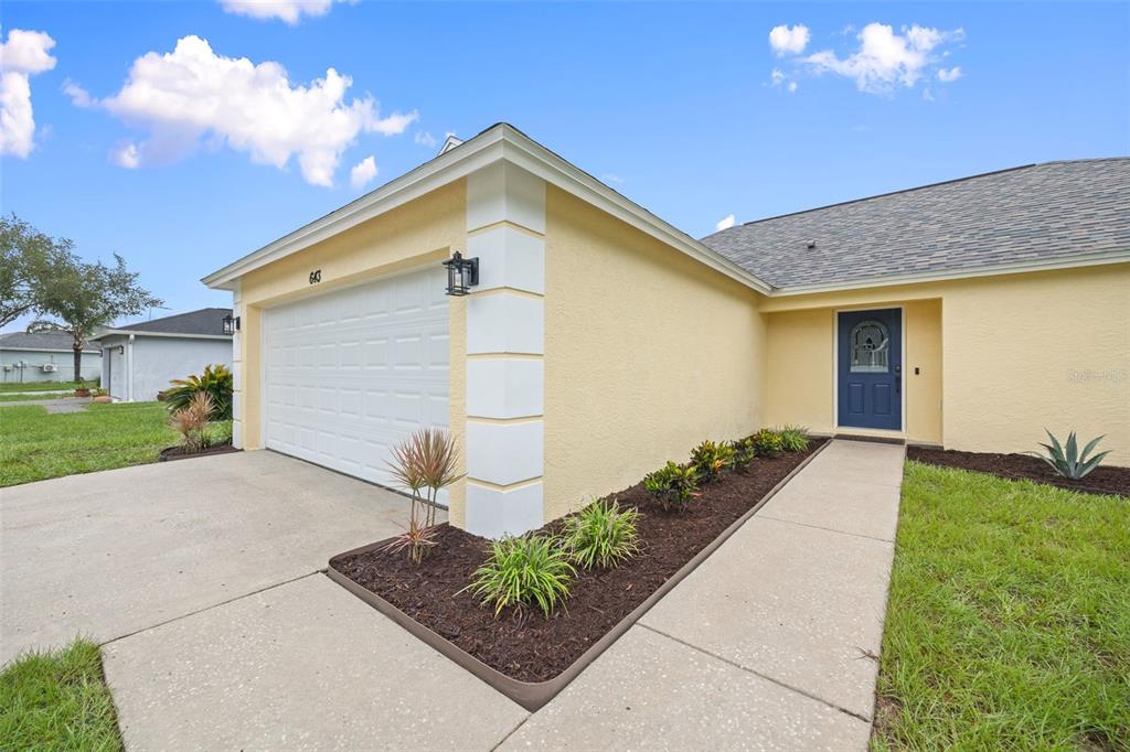 A yellow house exterior features a white garage door, a blue front door, and landscaping — 643 LAKEMONT DR, BRANDON, FL