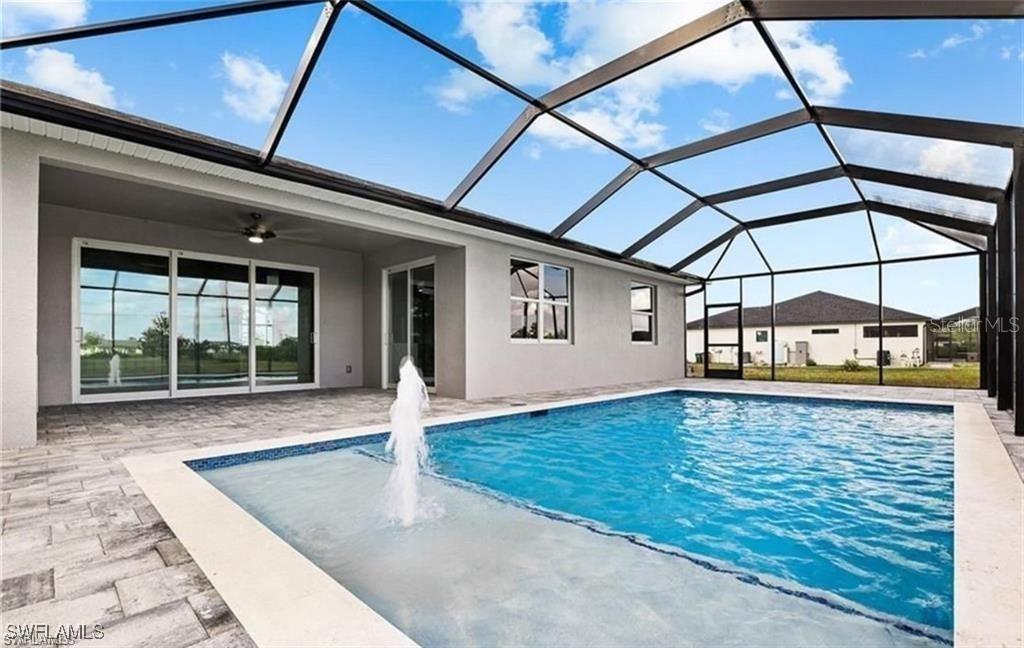 A swimming pool with a fountain sits inside a screened-in lanai behind a house — 925 NW 9TH AVENUE, CAPE CORAL, FL