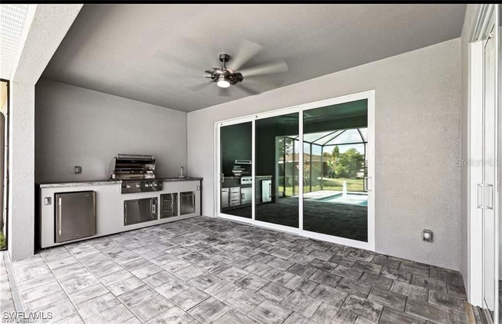 A covered outdoor patio features a built-in kitchen, tile flooring, and sliding glass doors — 925 NW 9TH AVENUE, CAPE CORAL, FL