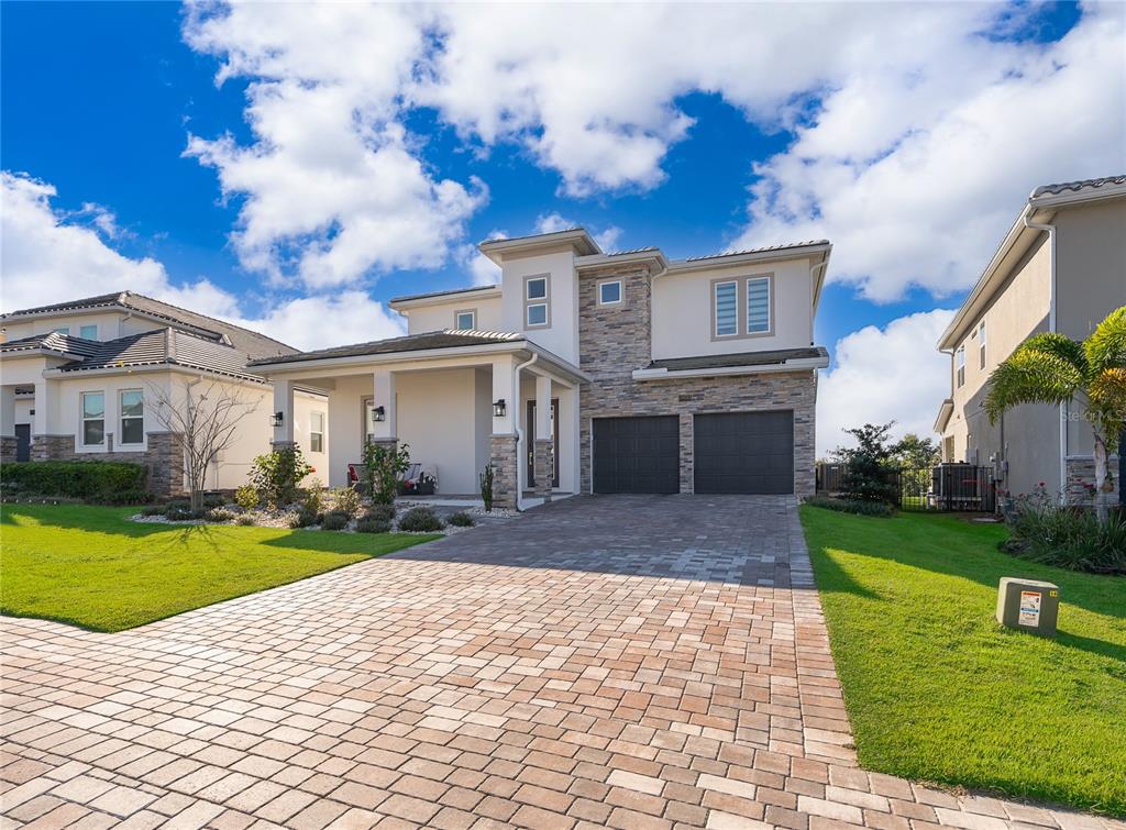 A two-story house with a stone facade, a paved driveway, and a covered front porch — 16033 VOLTERRA POINT, BELLA COLLINA, FL