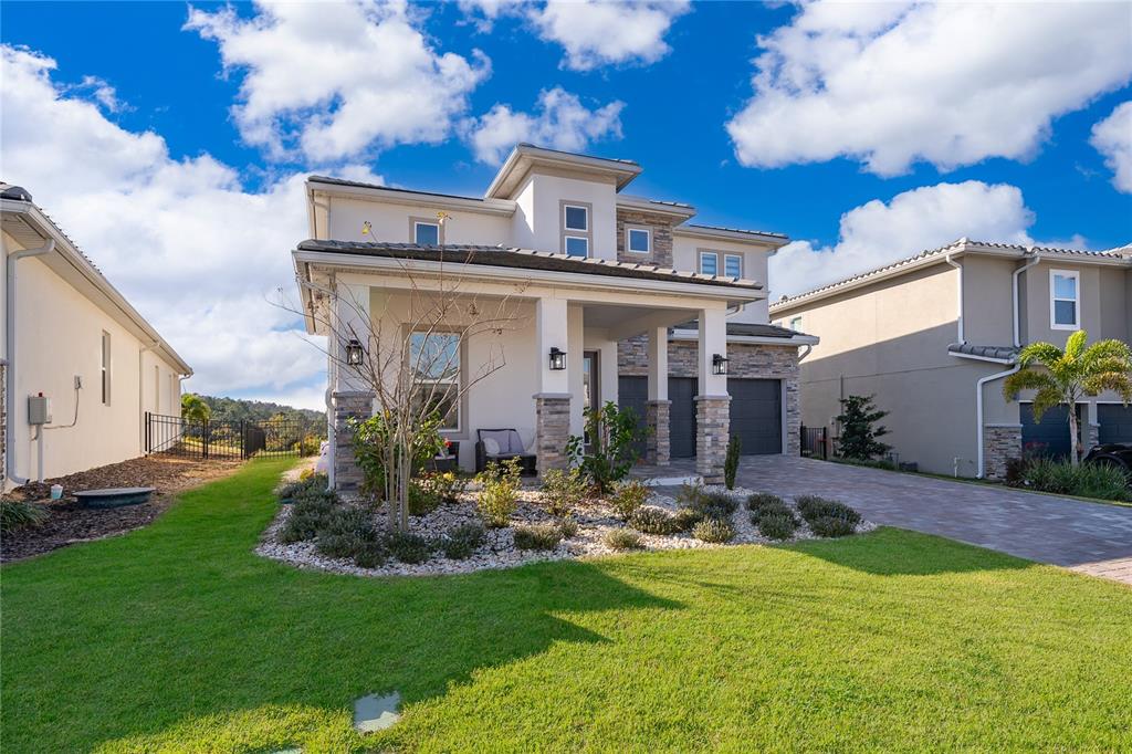 A two-story house with a stone-accented facade, covered porch, and a paved driveway — 16033 VOLTERRA POINT, BELLA COLLINA, FL