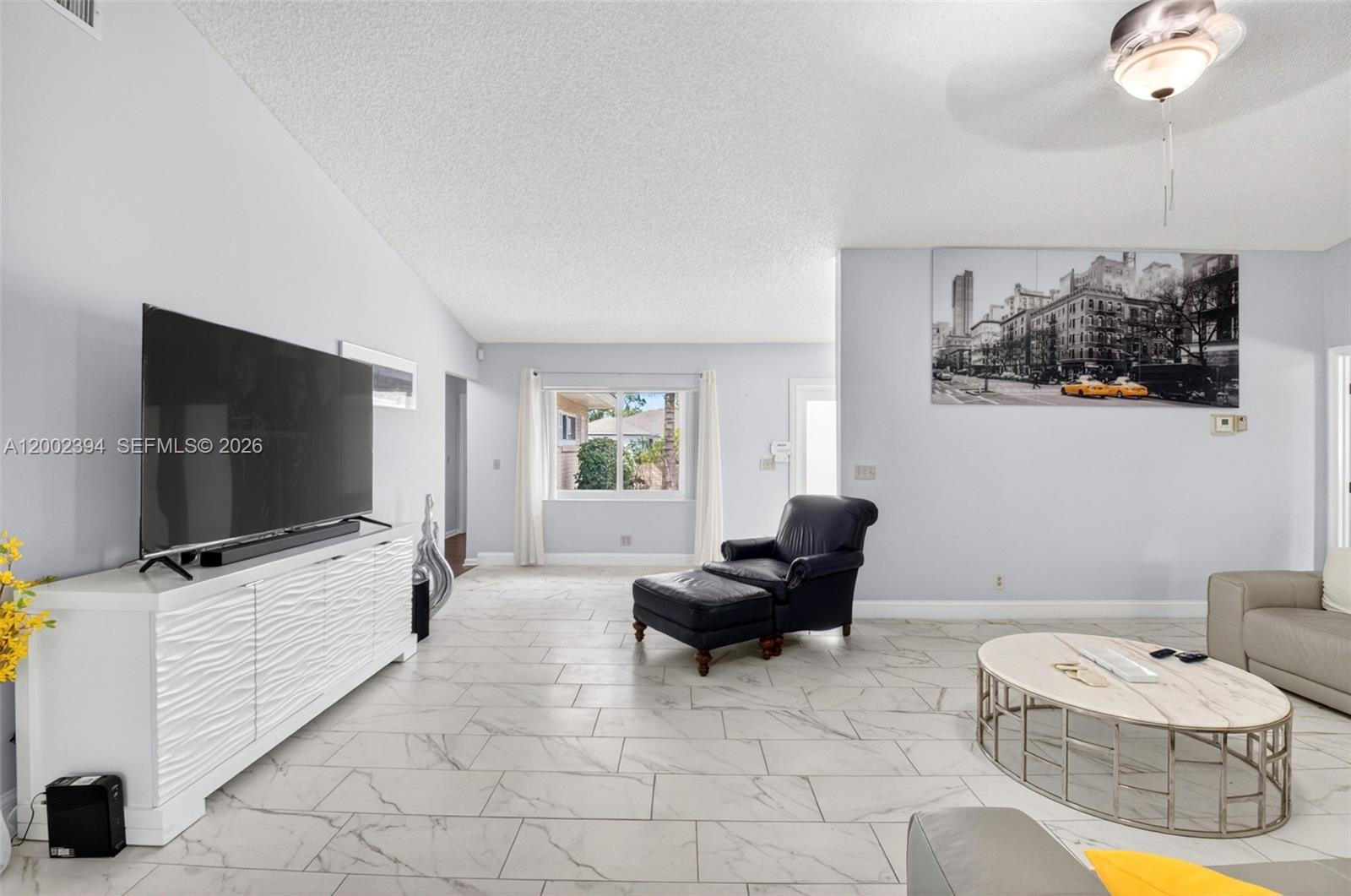 A living room features white tile flooring, a large television, and a black leather chair — 10982 S Greentrail Dr S, Boynton Beach FL 33436, BOYNTON BEACH, FL